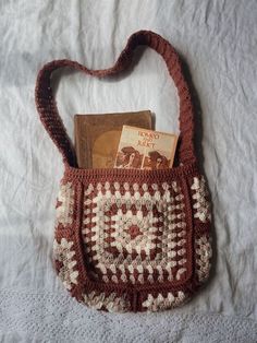 a crocheted purse sitting on top of a bed next to an open book