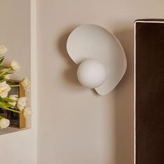 a vase with white flowers sitting next to a wall mounted light on the side of a wall