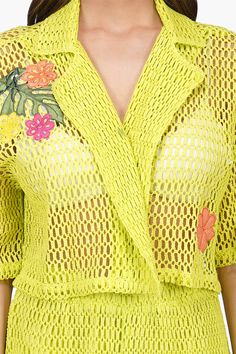 a woman wearing a bright yellow dress with flowers on the chest and sleeves, standing in front of a white background