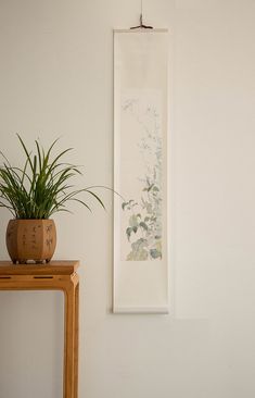 a potted plant sitting on top of a wooden table next to a wall hanging