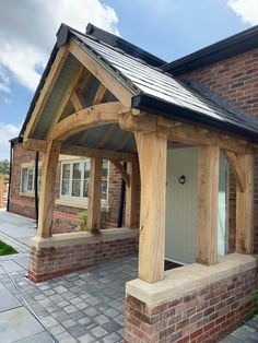 a brick house with a wooden porch and covered front door, sitting on a stone patio