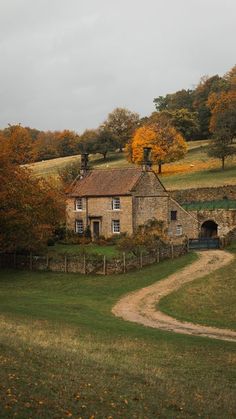 an old stone house in the middle of a field with trees and grass around it