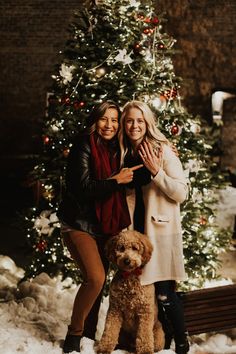 two women standing next to each other in front of a christmas tree with a dog