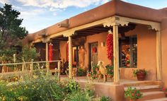 an adobe style house with red flowers on the porch