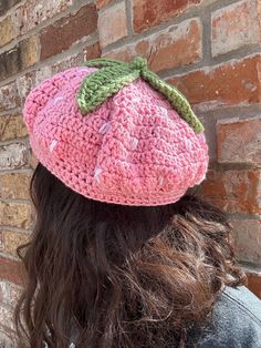 a woman wearing a pink crocheted hat with a green leaf on the top