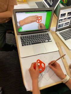 two people are working on an object in front of their laptops