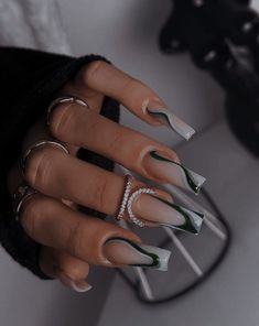 a manicured hand with green and white nail designs on it's fingers, holding a ring