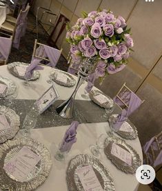 the table is set with silver plates and purple flowers