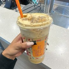 a person holding up a cup with ice cream in it and an orange straw sticking out of the top