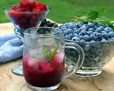 two glasses filled with fruit sitting on top of a wooden table next to blueberries and raspberries