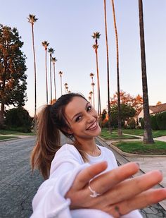 a woman is holding out her hand in front of palm trees on the side walk