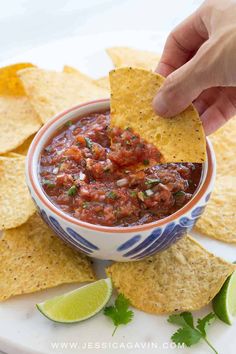 a hand dipping a tortilla chip into a bowl of salsa