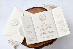 an open white wedding card on top of a wooden table next to flowers and paper