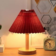 a red lamp sitting on top of a wooden table next to a small alarm clock