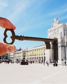 a person holding an old key in front of a building with people walking around it