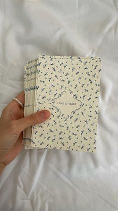 a hand holding an open book on top of a white sheet covered in blue flowers