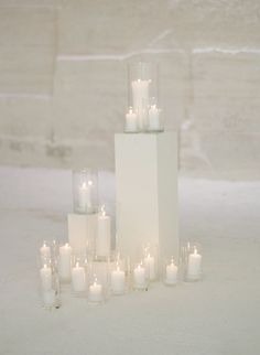 several tall white candles sitting next to each other in front of a brick wall and floor