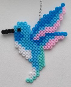 a blue and pink bird made out of legos on a silver chain hanging from a white wall