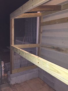 a chicken coop built into the side of a building with wooden posts and mesh doors