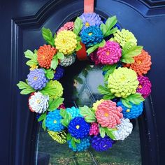 a colorful wreath made out of fake flowers on a blue front door with green leaves