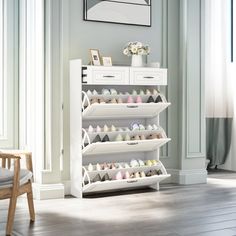 a white shoe rack filled with lots of pairs of shoes next to a chair and window