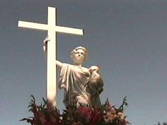 a statue of jesus holding the cross on top of a building with flowers around it