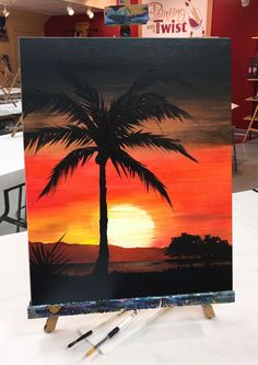 a palm tree painted on an easel in front of a red and orange sunset