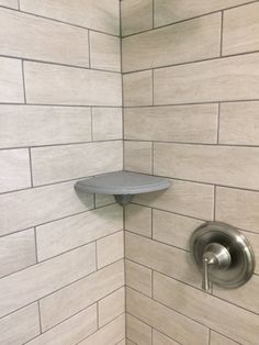 the corner of a shower with white tile and silver faucet on the wall