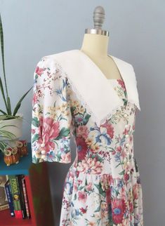 Vintage cottagecore dress from the 70's era! Colorful cabbage rose floral print in red, green, and blue. V-neck with removable panel, short pleated sleeves with buttons, puffed shoulders, and large white lace trimmed prairie collar. Button up front bodice, v-shaped gathered low waist with midi length full skirt. Removable shoulder pads. Step in and button front. Perfect for a spring party! Fits like a modern medium. Please check the measurements below: MEASUREMENTS--Taken with garment laying fla Spring Floral Print Fitted Prairie Dress, Short Sleeve Prairie Dress For Spring Garden Party, Vintage Floral Print Short Sleeve Prairie Dress, Vintage Short Sleeve Prairie Dress With Floral Print, Cottagecore Floral Prairie Dress For Summer, Spring Cottagecore Vintage Dress With Short Sleeves, Cottagecore Vintage Short Sleeve Dress For Spring, Vintage Spring Prairie Dress With Ditsy Floral Print, Vintage Prairie Dress With Ditsy Floral Print For Spring