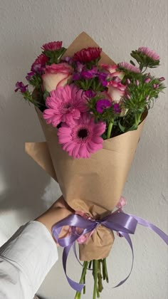 a person holding a bouquet of flowers in front of a white wall with purple ribbons