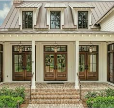 a white house with two brown doors and steps leading up to the front door is surrounded by greenery