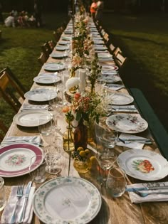 a long table set with plates and silverware for an outdoor dinner in the evening