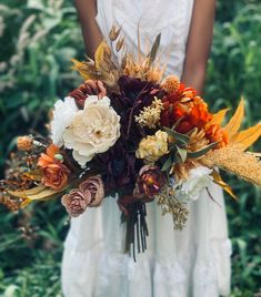 a woman in a white dress holding a large bouquet of flowers and grasses with her hands behind her back