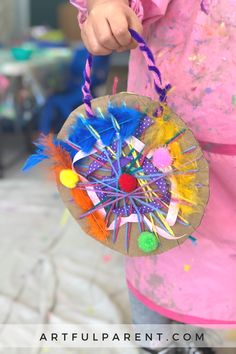 a child holding a paper plate with colorful feathers on it and a string attached to the top