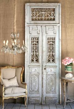 an old white door sitting next to a chair and table with flowers on top of it