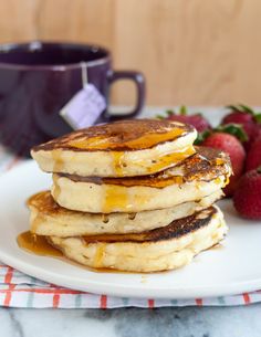 stack of pancakes with syrup and strawberries on the side