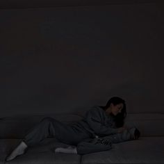 a woman laying on top of a couch in the dark with her feet up and head down