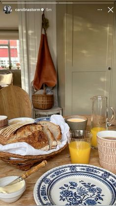 a table topped with plates and cups filled with breakfast food next to a basket full of orange juice