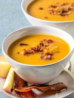 two white bowls filled with soup and bacon on top of a plate next to an apple slice