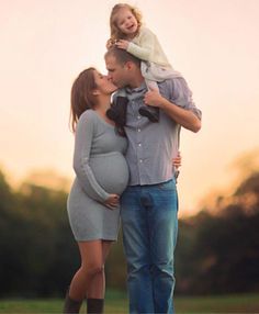 a man and woman holding a baby girl in their arms as the sun sets behind them