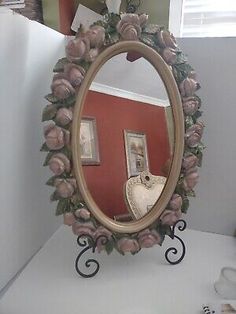 there is a mirror with roses on it in the corner next to a shelf and pictures