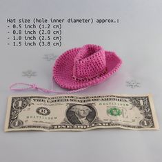 a pink crocheted hat sitting on top of a one dollar bill next to it