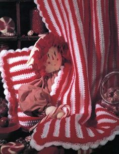 a teddy bear is wrapped in a red and white striped blanket on a chair next to a wine glass