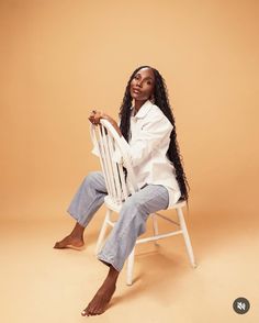 a woman sitting in a white chair with her legs crossed and looking at the camera