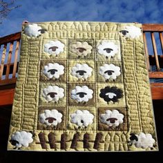 a quilted wall hanging on the side of a wooden fence with sheep in it