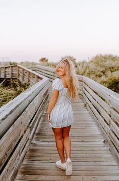 a woman walking across a wooden bridge in the sand and grass, with her hair blowing in the wind