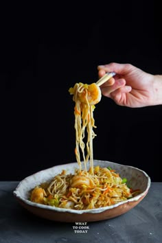 someone is eating noodles with chopsticks in a white bowl on a black surface