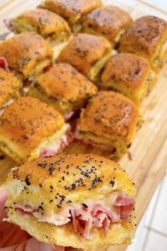 a ham and cheese slider cut in half on a cutting board with other sliders behind it