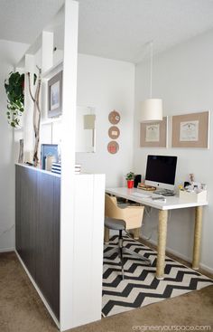 a desk with a computer on top of it in front of a wall mounted plant