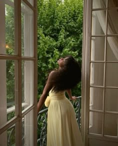 a woman in a yellow dress looking out an open window